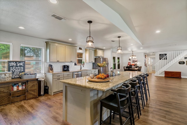 kitchen featuring decorative light fixtures, wood-type flooring, stainless steel dishwasher, and a kitchen island