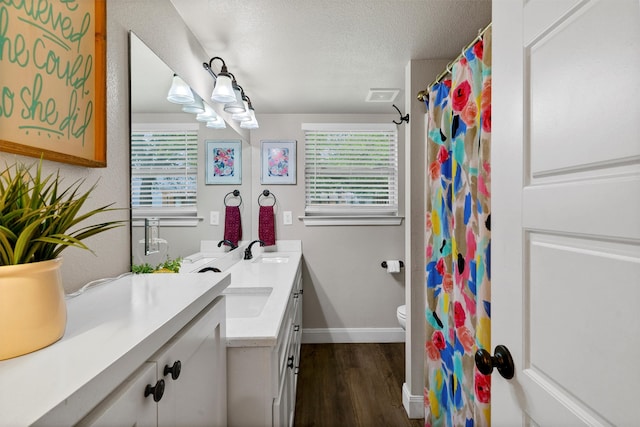 bathroom with a textured ceiling, dual bowl vanity, hardwood / wood-style floors, and toilet