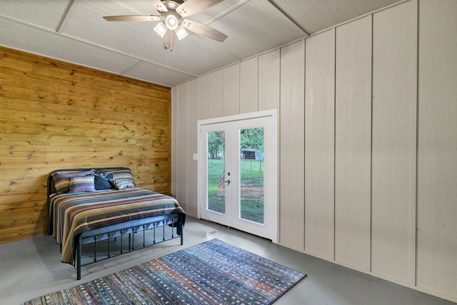 bedroom with wooden walls, concrete floors, ceiling fan, and french doors