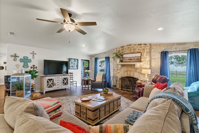 living room featuring a textured ceiling, a stone fireplace, ceiling fan, and hardwood / wood-style floors