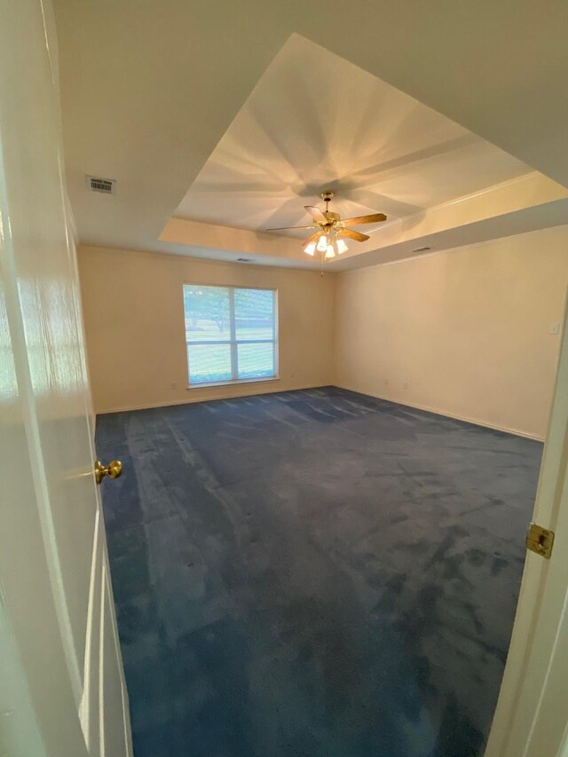 carpeted empty room with ceiling fan and a raised ceiling