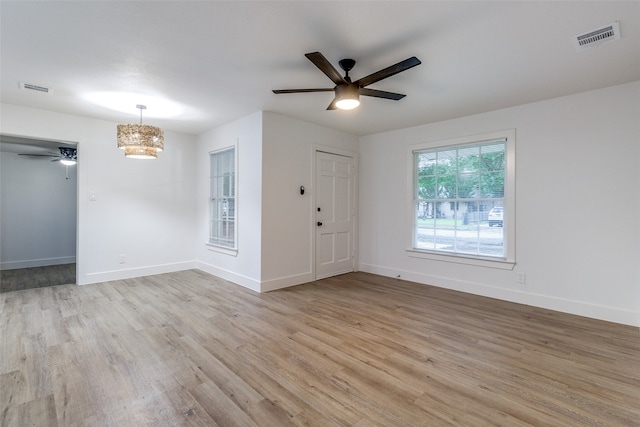 empty room with ceiling fan with notable chandelier and light wood-type flooring