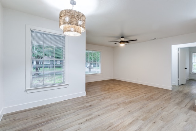 empty room featuring ceiling fan with notable chandelier and light hardwood / wood-style floors