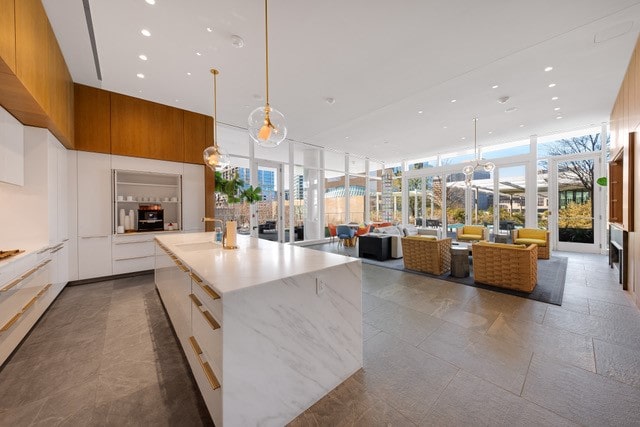 kitchen featuring light stone countertops, floor to ceiling windows, a spacious island, white cabinets, and dark tile floors