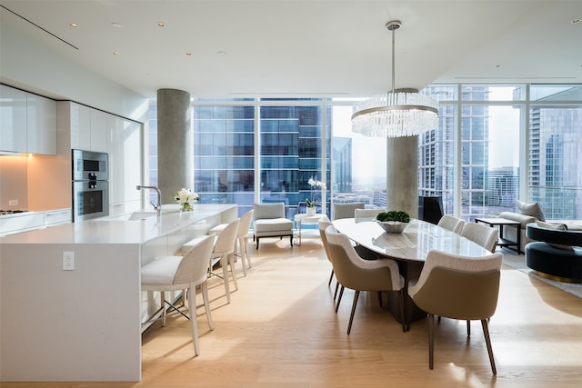 dining space with a wall of windows, light hardwood / wood-style flooring, sink, and a chandelier