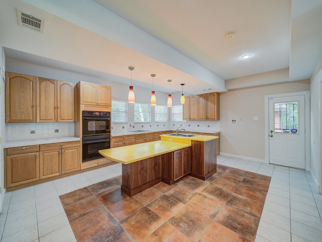 kitchen with hanging light fixtures, tasteful backsplash, a kitchen island with sink, black appliances, and sink