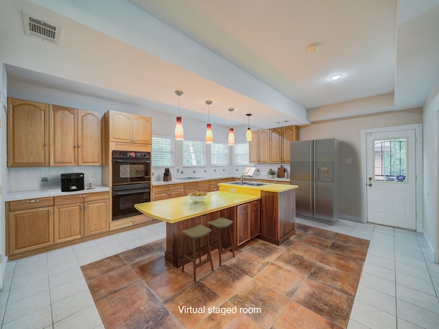 kitchen with an island with sink, black appliances, backsplash, hanging light fixtures, and sink