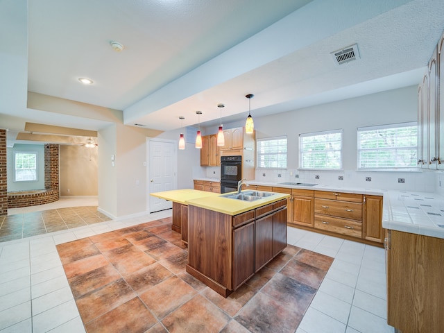 kitchen featuring backsplash, hanging light fixtures, a center island with sink, black appliances, and sink