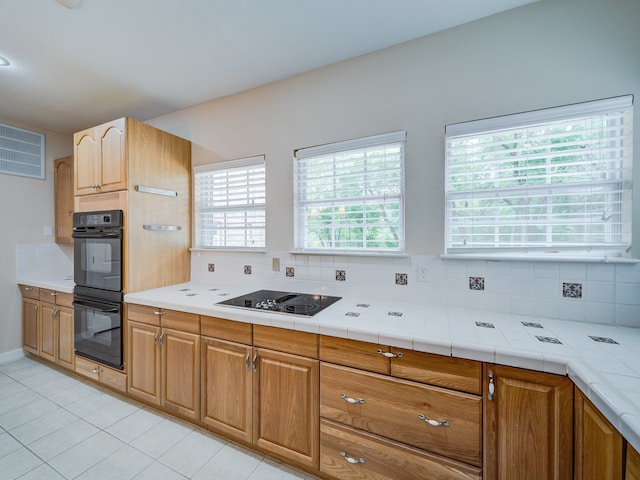 kitchen featuring tile counters, black appliances, tasteful backsplash, and light tile floors