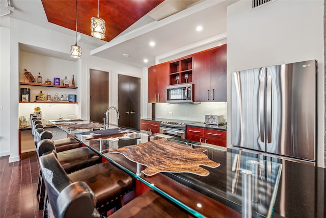 kitchen with appliances with stainless steel finishes, a breakfast bar, tasteful backsplash, dark hardwood / wood-style flooring, and pendant lighting