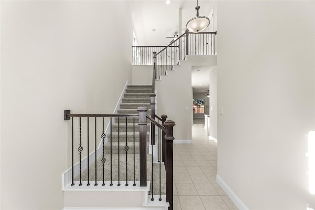 stairs with ceiling fan, tile patterned flooring, and a high ceiling