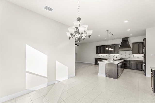 kitchen featuring custom exhaust hood, sink, decorative light fixtures, an island with sink, and dark brown cabinets