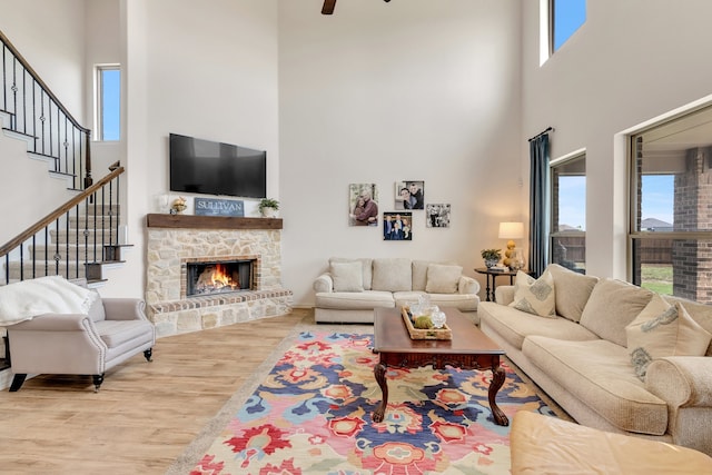 living room featuring a stone fireplace, a healthy amount of sunlight, a high ceiling, and light wood-type flooring