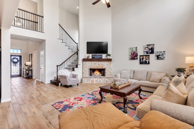 living room featuring ceiling fan, wood-type flooring, a fireplace, and a high ceiling