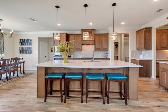 kitchen with premium range hood, a large island with sink, and decorative light fixtures