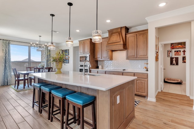 kitchen with sink, stainless steel microwave, hanging light fixtures, premium range hood, and a large island with sink