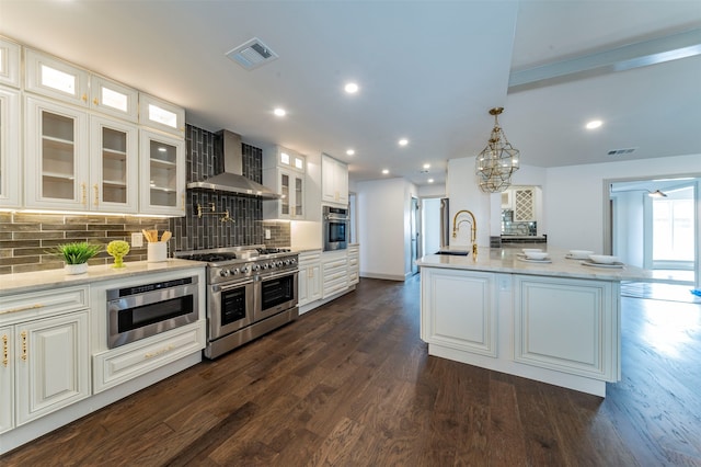 kitchen with appliances with stainless steel finishes, tasteful backsplash, wall chimney range hood, white cabinetry, and dark wood-type flooring