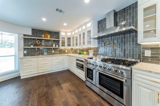 kitchen with appliances with stainless steel finishes, tasteful backsplash, wall chimney exhaust hood, white cabinetry, and dark hardwood / wood-style flooring