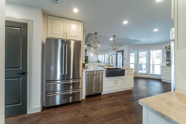 kitchen with pendant lighting, dark wood-type flooring, kitchen peninsula, appliances with stainless steel finishes, and sink