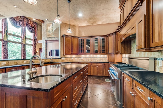 kitchen featuring high end stainless steel range oven, glass insert cabinets, a sink, and a center island with sink