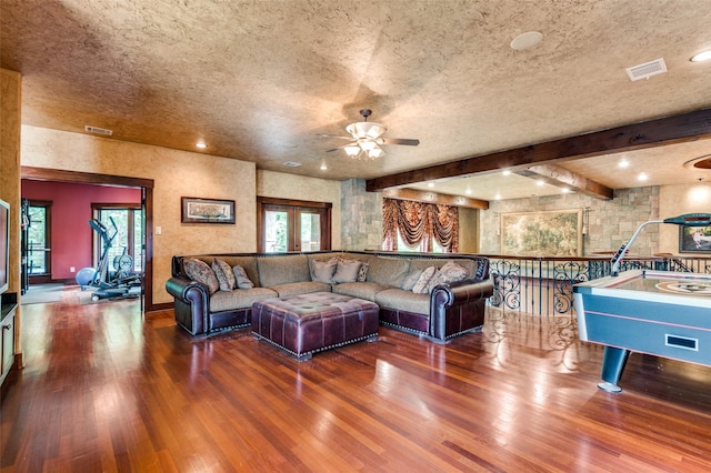 living area featuring beam ceiling, visible vents, a textured ceiling, and wood finished floors