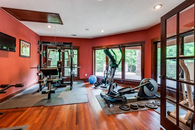 exercise area featuring attic access, visible vents, baseboards, and wood finished floors