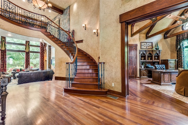 staircase with high vaulted ceiling, hardwood / wood-style floors, beam ceiling, and a notable chandelier