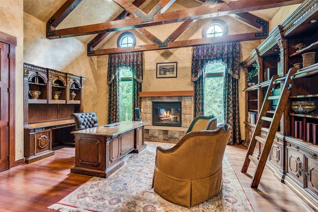 office space with beamed ceiling, high vaulted ceiling, light wood-type flooring, and a stone fireplace