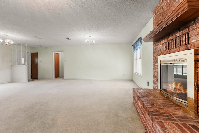 unfurnished living room with a textured ceiling, a brick fireplace, carpet floors, and an inviting chandelier