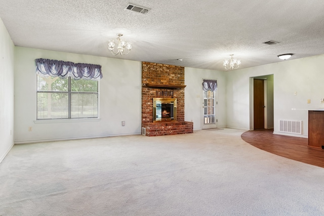 unfurnished living room with a fireplace, an inviting chandelier, a textured ceiling, and carpet flooring