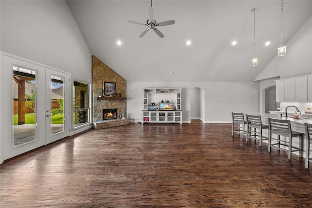 unfurnished living room with high vaulted ceiling, ceiling fan, dark hardwood / wood-style flooring, and a stone fireplace