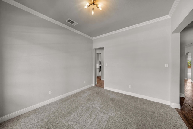 empty room with a notable chandelier, crown molding, and dark carpet