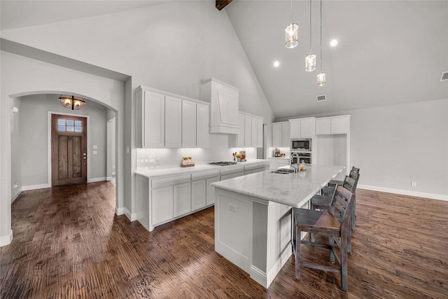 kitchen with stainless steel appliances, high vaulted ceiling, white cabinets, and a kitchen island with sink