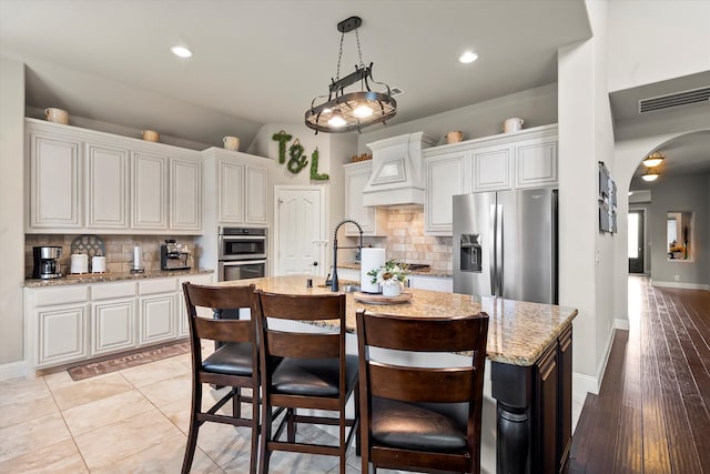 kitchen with custom exhaust hood, white cabinets, stainless steel appliances, and light hardwood / wood-style floors