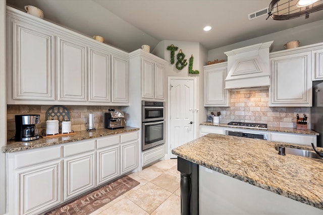 kitchen with light stone countertops, light tile patterned floors, backsplash, premium range hood, and white cabinets