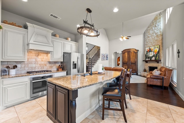 kitchen featuring custom exhaust hood, light stone counters, a stone fireplace, appliances with stainless steel finishes, and lofted ceiling