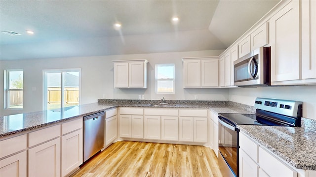 kitchen with stainless steel appliances, plenty of natural light, white cabinets, and light hardwood / wood-style flooring