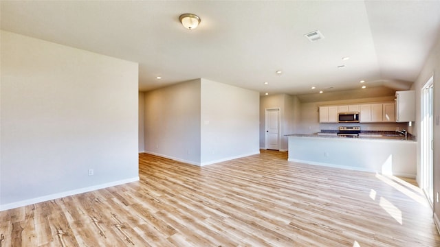 unfurnished living room with light wood-type flooring, sink, and lofted ceiling