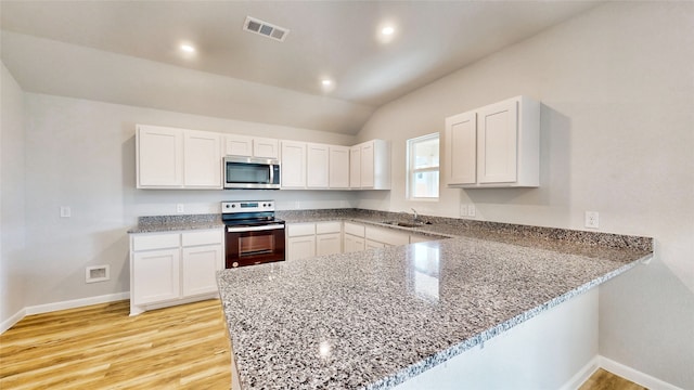 kitchen with light wood-type flooring, vaulted ceiling, kitchen peninsula, appliances with stainless steel finishes, and white cabinetry