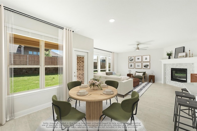 dining space featuring a ceiling fan, baseboards, light wood finished floors, and a tiled fireplace