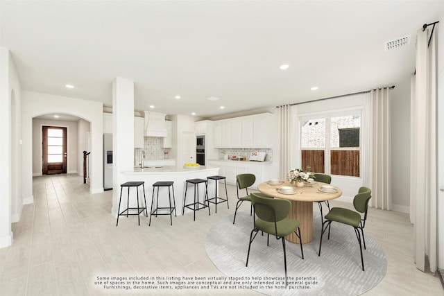 dining area with arched walkways, light wood-style flooring, recessed lighting, visible vents, and baseboards