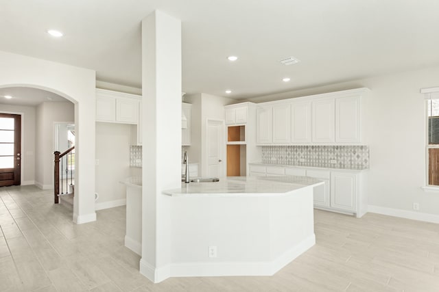 kitchen featuring arched walkways, a sink, white cabinetry, light countertops, and decorative backsplash