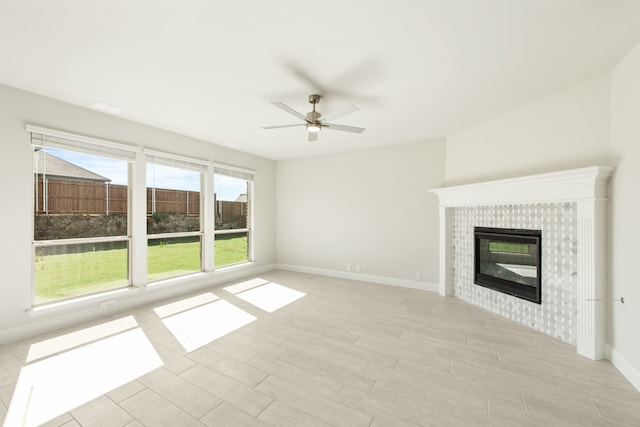 unfurnished living room with baseboards, a tiled fireplace, a ceiling fan, and light wood-style floors