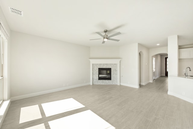 unfurnished living room featuring arched walkways, a fireplace, visible vents, baseboards, and a ceiling fan