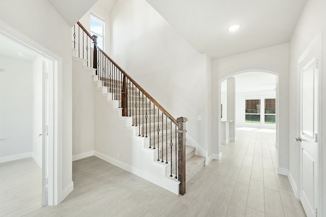 stairs with arched walkways, wood finish floors, and baseboards