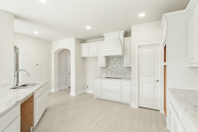 kitchen featuring custom range hood, arched walkways, white cabinets, and a sink