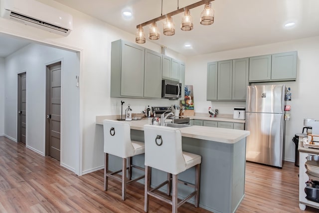 kitchen featuring hanging light fixtures, light hardwood / wood-style flooring, stainless steel appliances, kitchen peninsula, and a wall mounted AC