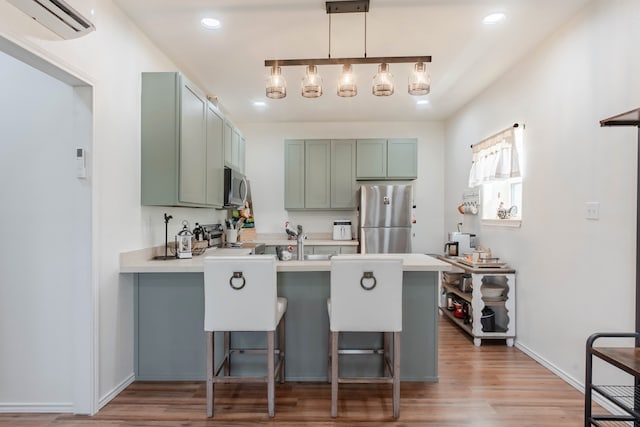 kitchen with kitchen peninsula, stainless steel appliances, a kitchen breakfast bar, hardwood / wood-style floors, and green cabinets