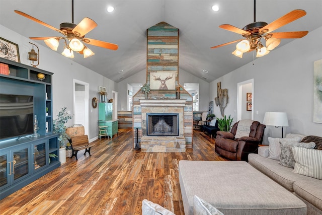 living room featuring hardwood / wood-style floors, vaulted ceiling, ceiling fan, and a stone fireplace