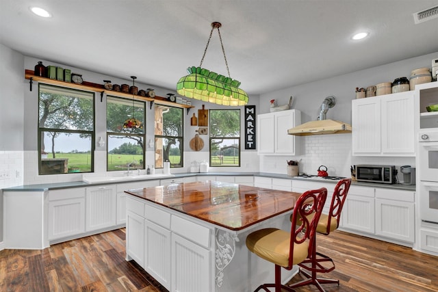 kitchen with a center island, wall chimney exhaust hood, tasteful backsplash, white cabinetry, and dark hardwood / wood-style flooring